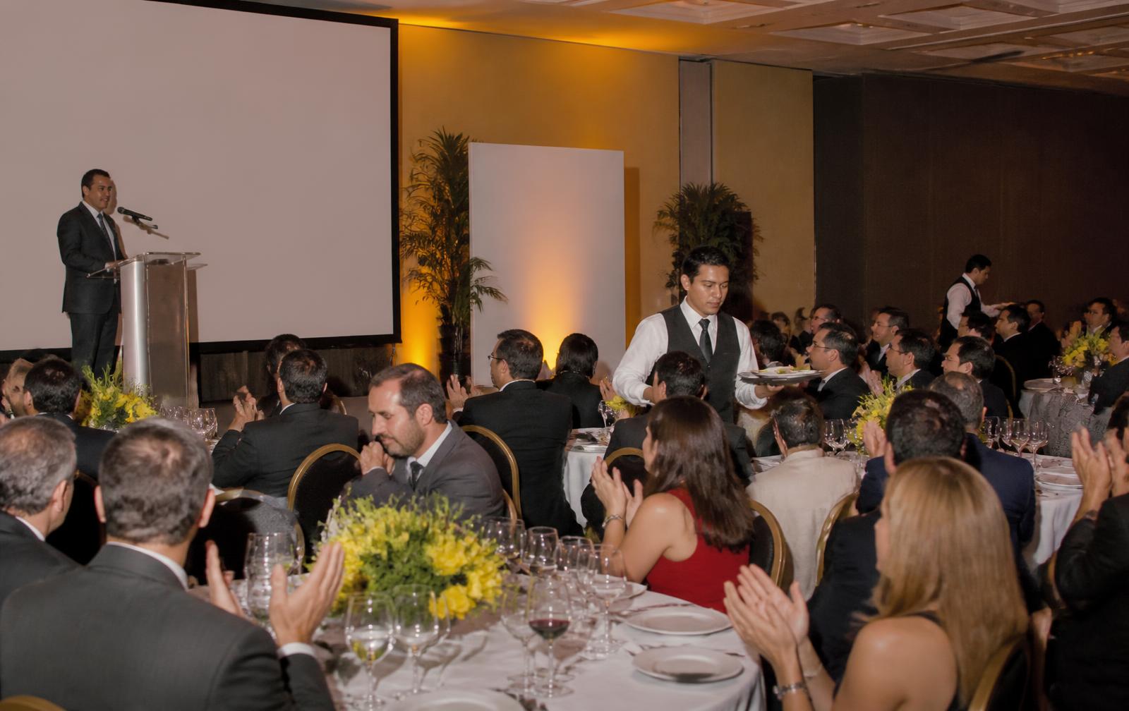 Gala corporativa de noche con tarima iluminada y mesas con velas