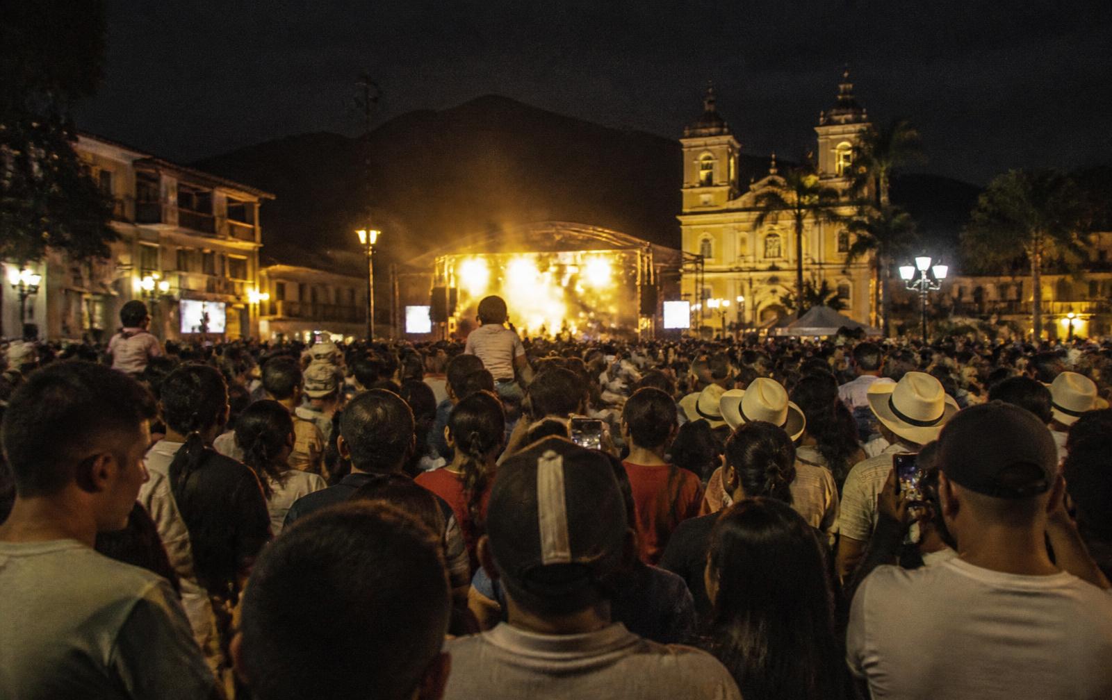 Público con las manos en alto frente a una tarima en un festival cultural nocturno